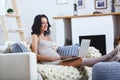 Beautiful young pregnant woman with laptop sitting on sofa at home Royalty Free Stock Photo