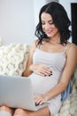 Beautiful young pregnant woman with laptop sitting on sofa at home Royalty Free Stock Photo