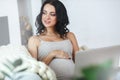 Beautiful young pregnant woman with laptop sitting on sofa at home Royalty Free Stock Photo