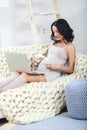 Beautiful young pregnant woman with laptop sitting on sofa at home Royalty Free Stock Photo