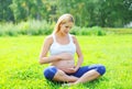 Beautiful young pregnant woman sitting on grass doing yoga in sunny summer Royalty Free Stock Photo