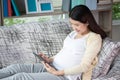 Beautiful young pregnant woman smile and using tablet computer shopping online while lying on sofa at living room. Relax, rest