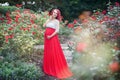 Beautiful young pregnant woman walking in the field of roses