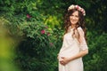 Beautiful young pregnant woman wearing white dress and floral wreath in the summer green park, summertime, pregnant girl. The Royalty Free Stock Photo