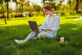 Beautiful young pretty redhead woman in park outdoors using laptop computer for study or work online using wireless Royalty Free Stock Photo