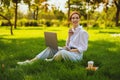 Beautiful young pretty redhead woman in park outdoors using laptop computer for study or work online, wireless earphones Royalty Free Stock Photo