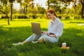Beautiful young pretty redhead woman in park outdoors using laptop computer for study or work online, wireless earphones Royalty Free Stock Photo