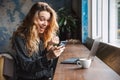 Beautiful young pretty woman sitting in cafe indoors using laptop computer and mobile phone Royalty Free Stock Photo