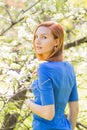 Beautiful young red-haired girl in blue dress among spring flowe