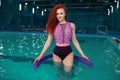 Beautiful young red-haired girl in a fashionable swimsuit in the style of the 80s stands with the noodles in her hands in the Royalty Free Stock Photo