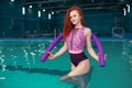 Beautiful young red-haired girl in a fashionable swimsuit in the style of the 80s stands with the noodles in her hands in the Royalty Free Stock Photo