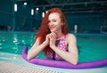 Beautiful young red-haired girl in a fashionable swimsuit in the style of the 80s stands with the noodles in her hands in the Royalty Free Stock Photo