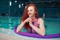 Beautiful young red-haired girl in a fashionable swimsuit in the style of the 80s stands with the noodles in her hands in the Royalty Free Stock Photo