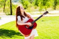 A beautiful young red-haired girl is laughing and playing guitar in a Park on a summer day. Royalty Free Stock Photo