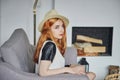Beautiful young red-haired girl sitting on the sofa in the living room against the background of the fireplace Royalty Free Stock Photo