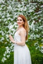 A beautiful young red-haired woman enjoys life in a spring blooming garden with a background of flowering trees. Dreamy pensive Royalty Free Stock Photo