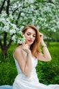 A beautiful young red-haired woman enjoys life in a spring blooming garden with a background of flowering trees. Dreamy pensive Royalty Free Stock Photo