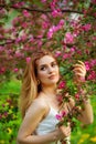 A beautiful young red-haired woman enjoys life in a spring blooming garden with a background of flowering trees. Young dreamy Royalty Free Stock Photo