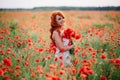 Beautiful young red-haired woman in poppy field holding a bouquet of poppies Royalty Free Stock Photo