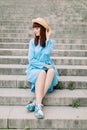 Beautiful young red haired woman wearing blue dress and hat, posing to camera while sitting on city stairs outdoors Royalty Free Stock Photo