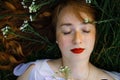 Beautiful young girl with long red curly hair. Girl with closed eyes lies on the green grass. view from above. Royalty Free Stock Photo