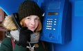 Beautiful young redhead girl in cold season outfit using street blue payphone. Royalty Free Stock Photo