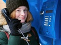 Beautiful young redhead girl in cold season outfit using street blue payphone. Royalty Free Stock Photo