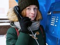 Beautiful young redhead girl in cold season outfit using street blue payphone. Royalty Free Stock Photo