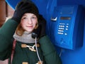 Beautiful young redhead girl in cold season outfit using street blue payphone. Royalty Free Stock Photo