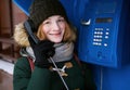 Beautiful young redhead girl in cold season outfit using street blue payphone. Royalty Free Stock Photo