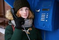 Beautiful young redhead girl in cold season outfit using street blue payphone. Royalty Free Stock Photo