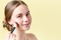 Beautiful young redhead woman with freckles contouring her cheekbones with make up brush. Beauty portrait