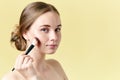 Beautiful young redhead woman with freckles contouring her cheekbones using make up brush. Beauty portrait.