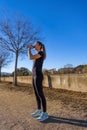 Beautiful young runner girl, beautifully illuminated by sunrise light, drinking water and hydrating from a bottle, dressed in