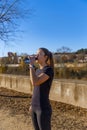 Beautiful young runner girl, beautifully illuminated by sunrise light, drinking water and hydrating from a bottle with her eyes