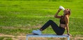 Beautiful young runner girl, tanned with long dark hair, sitting on a wooden bench, smiling and drinking from a bottle of water Royalty Free Stock Photo