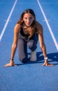 Beautiful young runner girl, tanned with long dark hair, smiling looking at camera at the starting line of a blue running track Royalty Free Stock Photo