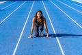 Beautiful young runner, tanned with long dark hair, smiling on a blue running track looking at the camera with her hands resting Royalty Free Stock Photo