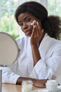 Young black girl applying moisturizing cream in front of mirror in bathroom. Royalty Free Stock Photo