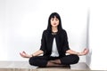 Beautiful young serious woman dressed in a black business suit sitting in lotus position on a floor in office, closed her eyes Royalty Free Stock Photo