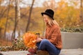 Beautiful young sexy blonde girl in a brown warm sweater, black felt hat, blue jeans and boots sits on a bench, cross-legged, Royalty Free Stock Photo