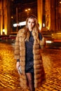 Beautiful young blonde wearing evening makeup in elegant fitting dress fashionable stylish expensive fur coat walk night stre