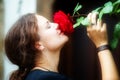 Beautiful young sexy dark-haired woman, with interesting classic profile puts her nose deep in red roses growing in the garden in Royalty Free Stock Photo