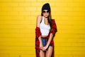Beautiful young hipster girl posing and smiling near urban yellow wall background in sunglasses. Royalty Free Stock Photo