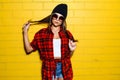 Beautiful young hipster girl posing and smiling near urban yellow wall background in sunglasses, red plaid shirt. Royalty Free Stock Photo