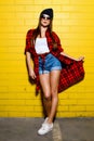 Beautiful young hipster girl posing and smiling near urban yellow wall background in sunglasses. Royalty Free Stock Photo