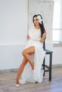 Beautiful young woman with dark hair in white dress sitting on chair in white Studio Royalty Free Stock Photo