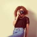 Beautiful young woman in jeans with a camera in the hands of curly hair in the Studio, retro filter