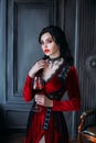 Beautiful young sexy woman vampire in medieval dark castle. Red gothic evening dress. Black wavy hair. Backdrop vintage Royalty Free Stock Photo