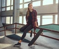 A beautiful young skateboarder girl wearing a checkered shirt sitting on a grind rail in skatepark indoors. Royalty Free Stock Photo